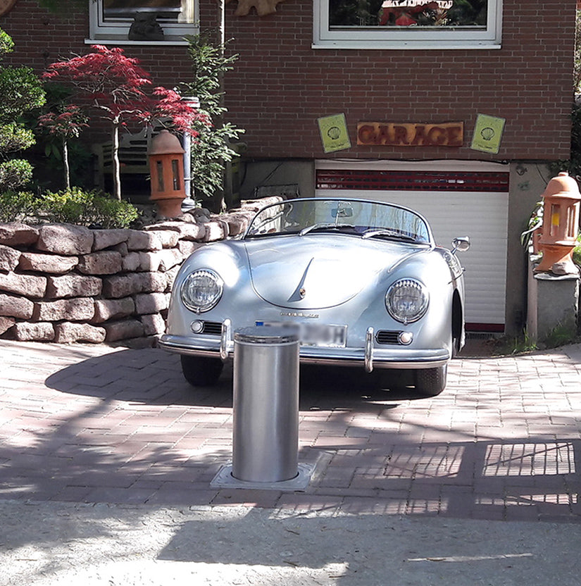 Silberner Porsche 356 vor einer Garage, davor ein ausgefahrener versenkbarer Edelstahl-Poller in der gepflasterten Einfahrt