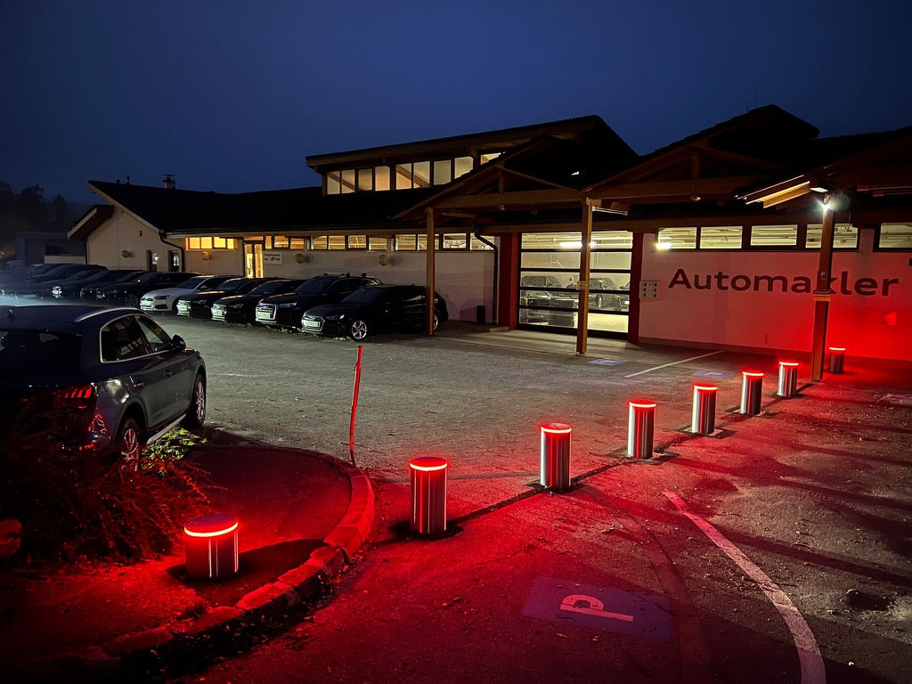Autohaus in Österreich bei Nacht: acht versenkbare Poller aus Edelstahl V4A mit rot leuchtenden LED-Ringen sichern den Ausstellungsplatz vor dem Gebäude