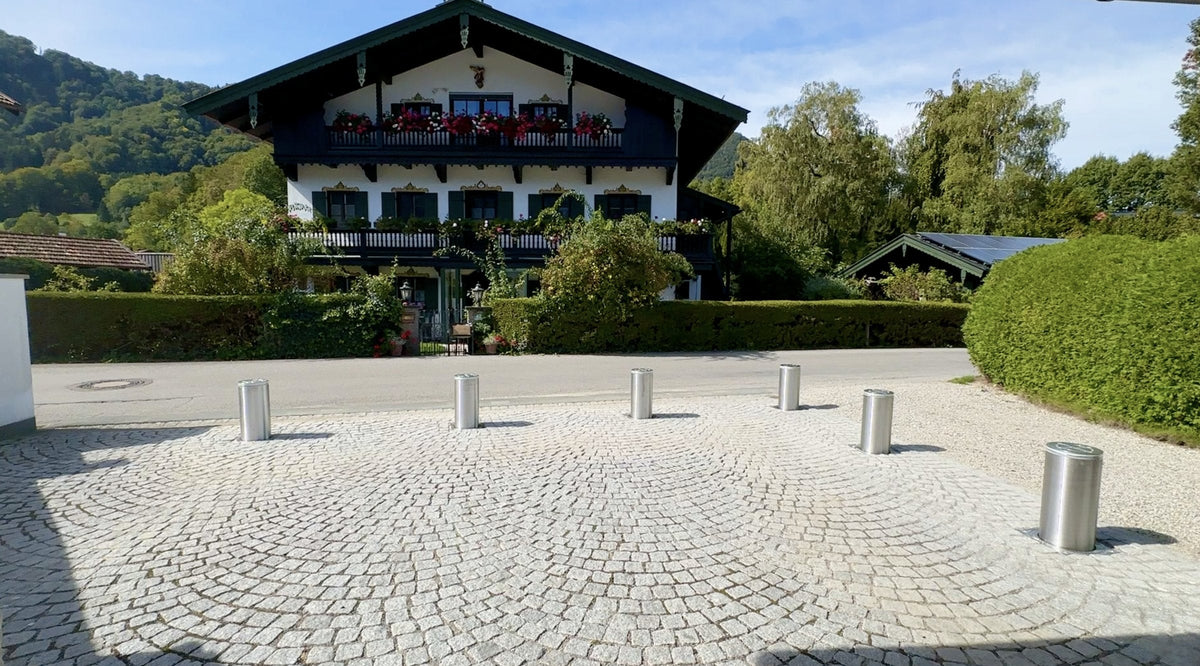 Sechs ausgefahrene versenkbare Edelstahl-Poller sichern eine Hofeinfahrt aus Granit-Kleinpflaster in Oberbayern