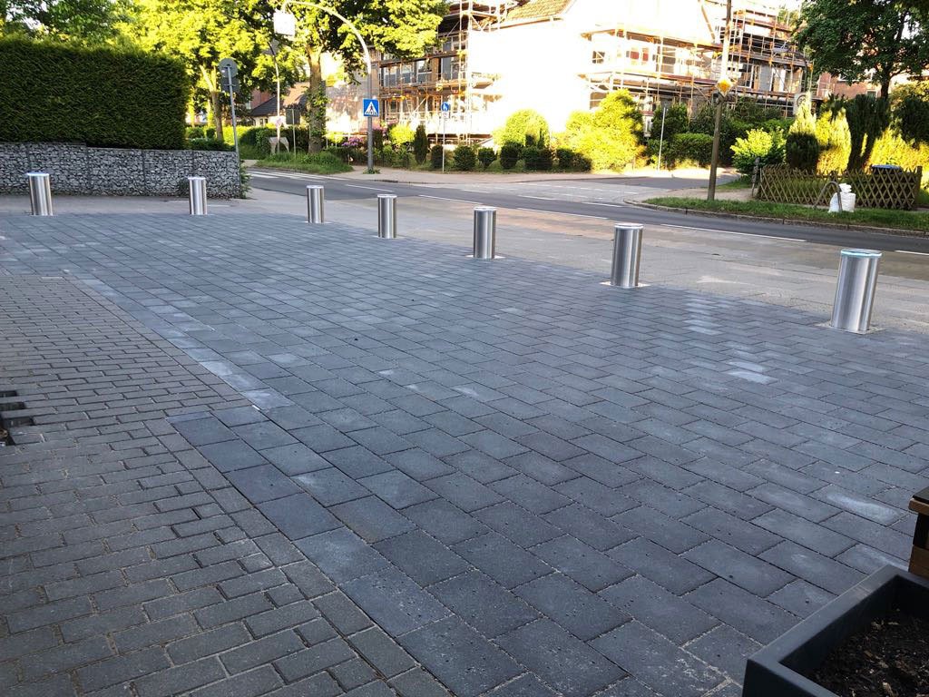 Sieben versenkbare Edelstahl-Poller sichern den Kundenparkplatz eines Raumausstatters in Hamburg zur Straße hin ab