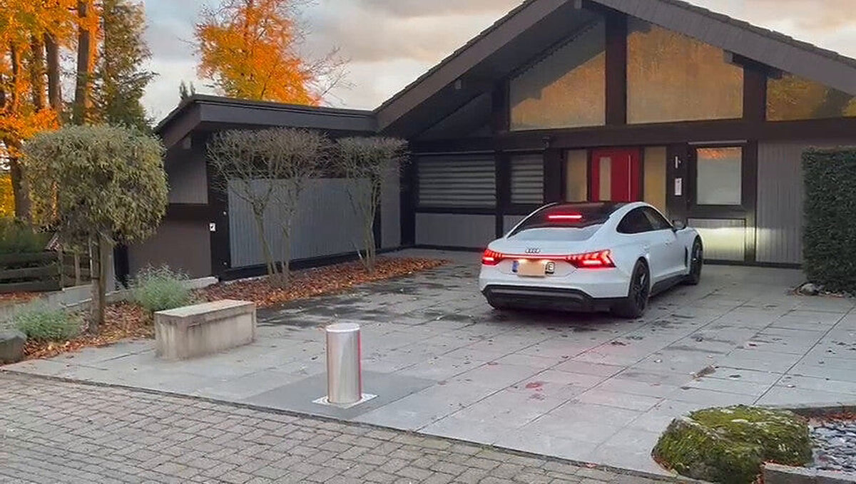 Versenkbarer Edelstahl-Poller mitten in der Hofeinfahrt eines Einfamilienhauses, dahinter ein geparktes Elektroauto
