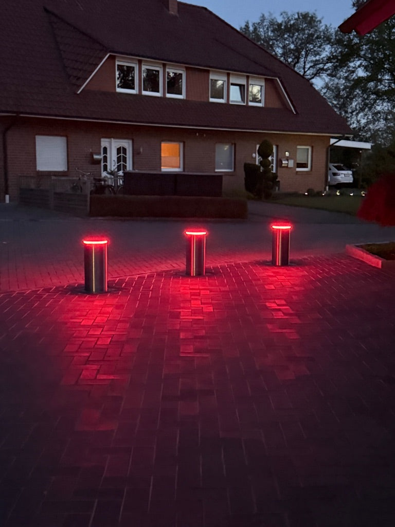 Drei versenkbare Poller mit roter LED-Beleuchtung an einer Einfahrt bei Dämmerung – Braun Antriebe