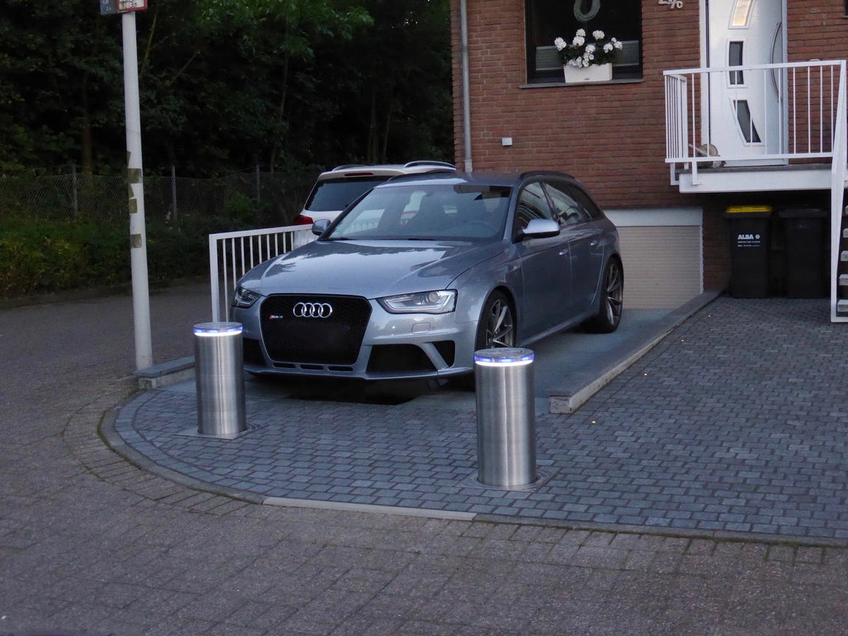 Zwei ausgefahrene versenkbare Edelstahl-Poller V4A mit Höhensicherung sperren die gepflasterte Einfahrt vor einer Garage mit Audi als Diebstahlschutz