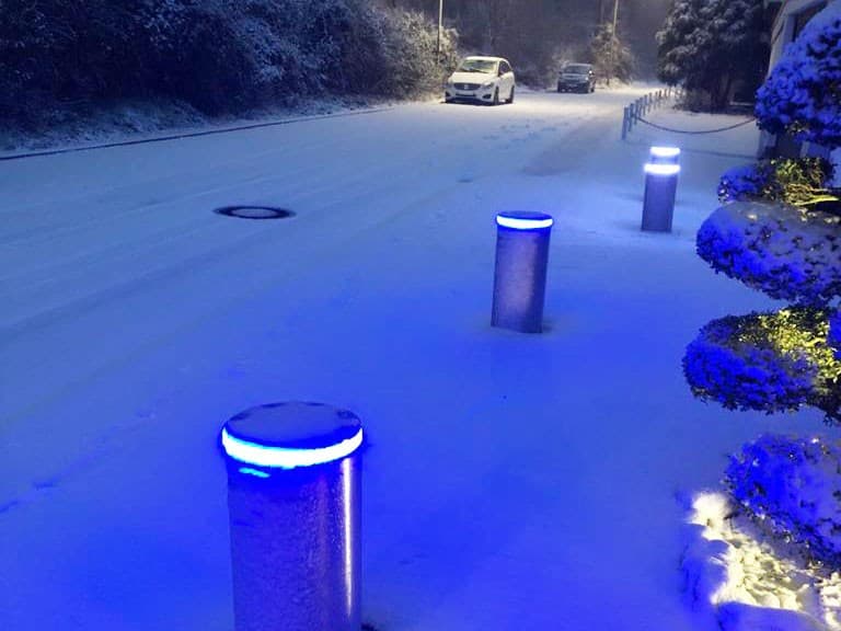 Ausgefahrene versenkbare Edelstahl-Poller mit blauem LED-Ring im Schnee vor einem Gebäude – Anprallschutz und Parkplatzsicherung