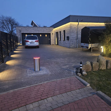 Versenkbarer Edelstahl-Poller mit rotem LED-Ring sichert abends die Einfahrt eines modernen Wohnhauses