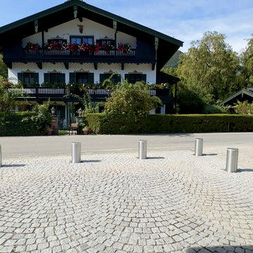Sechs ausgefahrene versenkbare Edelstahl-Poller sichern eine Hofeinfahrt aus Granit-Kleinpflaster in Oberbayern
