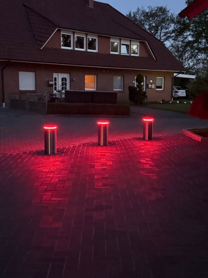 Drei versenkbare Poller mit roter LED-Beleuchtung an einer Einfahrt bei Dämmerung – Braun Antriebe
