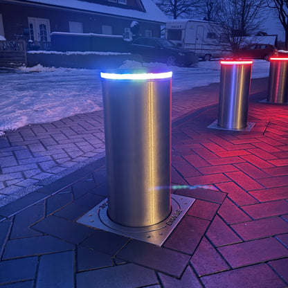 Versenkbarer Poller Edelstahl V4A mit LED-Lichtring an einer gepflasterten Einfahrt – pneumatisch, Braun Antriebe
