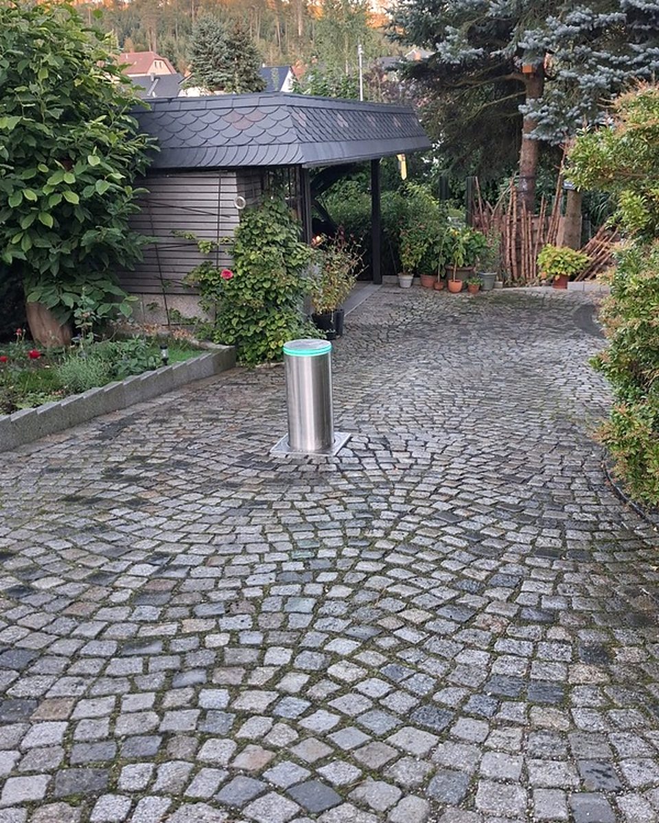 Versenkbarer Edelstahl-Poller mit grünem LED-Leuchtring in einer gepflasterten Hofeinfahrt – Braun Antriebe